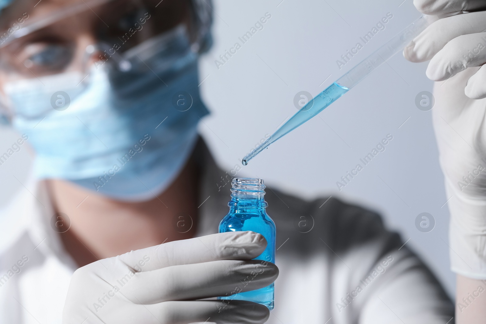 Photo of Scientist dripping liquid from pipette into glass bottle on light background, closeup