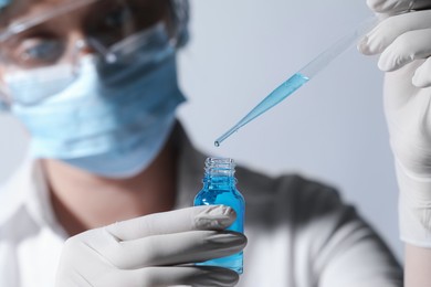 Photo of Scientist dripping liquid from pipette into glass bottle on light background, closeup