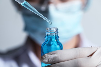 Photo of Scientist dripping liquid from pipette into glass bottle on light background, closeup