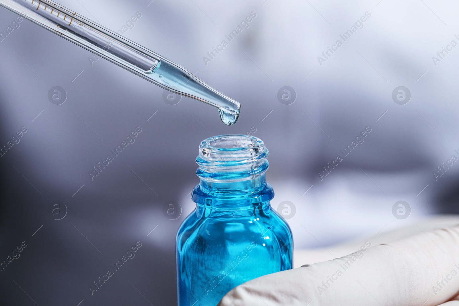 Photo of Scientist dripping liquid from pipette into bottle on light background, closeup