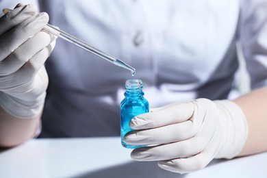 Scientist dripping liquid from pipette into glass bottle at white table, closeup