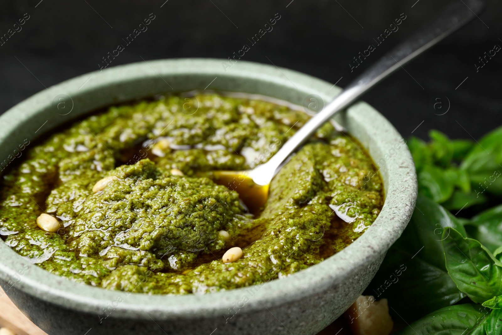 Photo of Tasty pesto sauce in bowl, spoon and basil on table, closeup