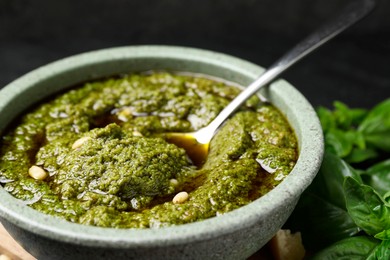 Tasty pesto sauce in bowl, spoon and basil on table, closeup