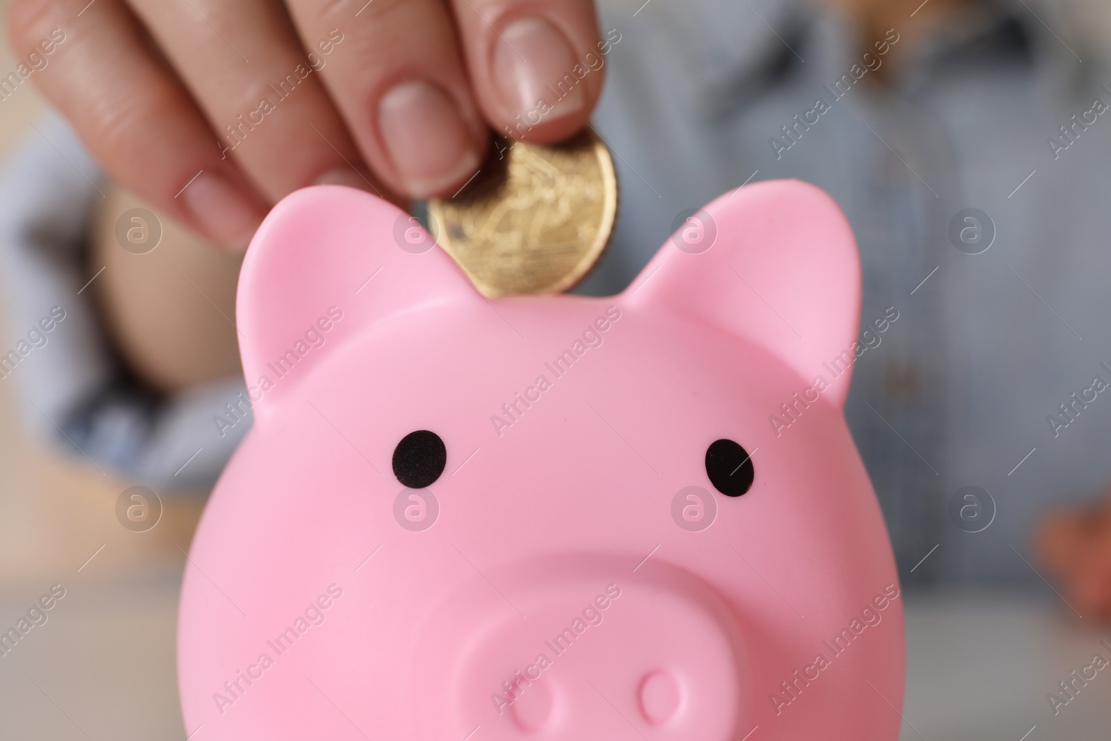 Photo of Woman putting coin into pink piggy bank at table, closeup