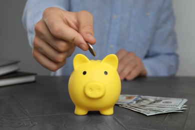 Photo of Man putting coin into yellow piggy bank at black table, closeup