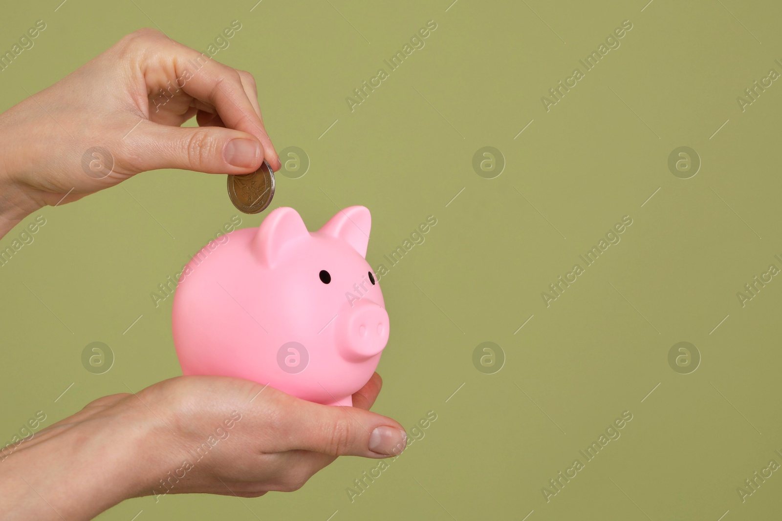 Photo of Woman putting coin into pink piggy bank on olive background, closeup. Space for text