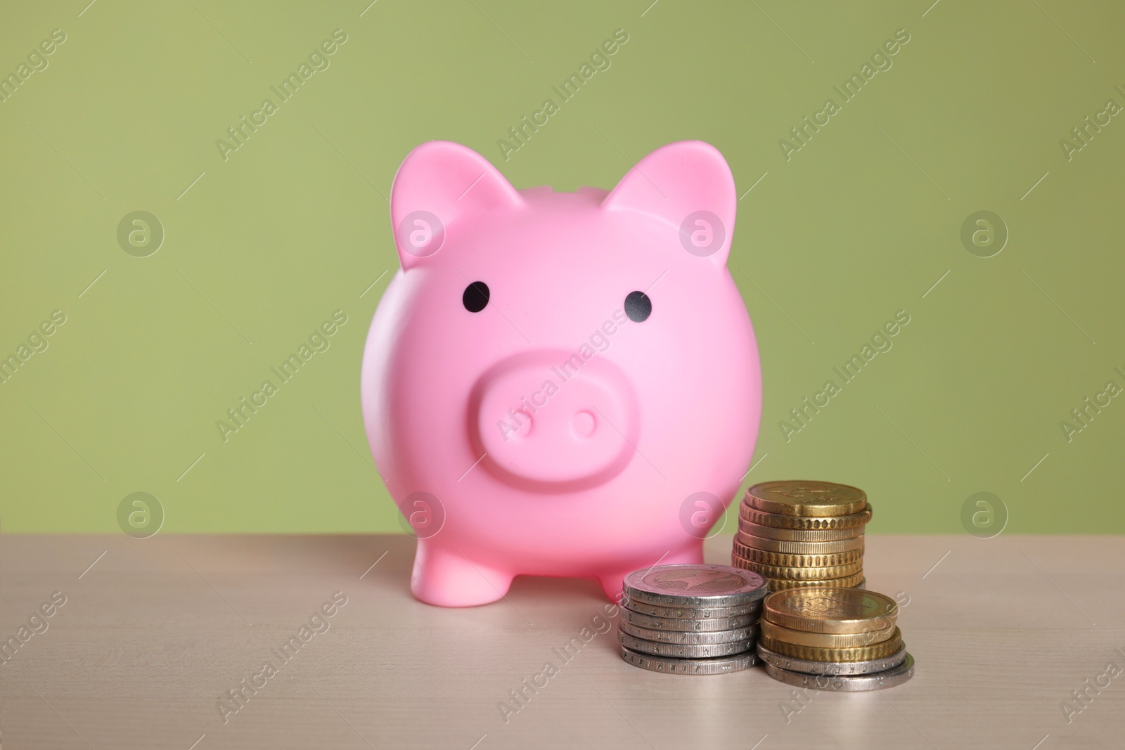 Photo of Pink piggy bank and coins on wooden table against olive background