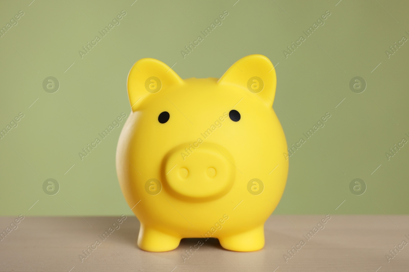 Photo of Yellow piggy bank on wooden table against olive background