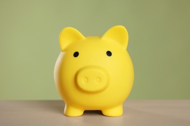 Photo of Yellow piggy bank on wooden table against olive background