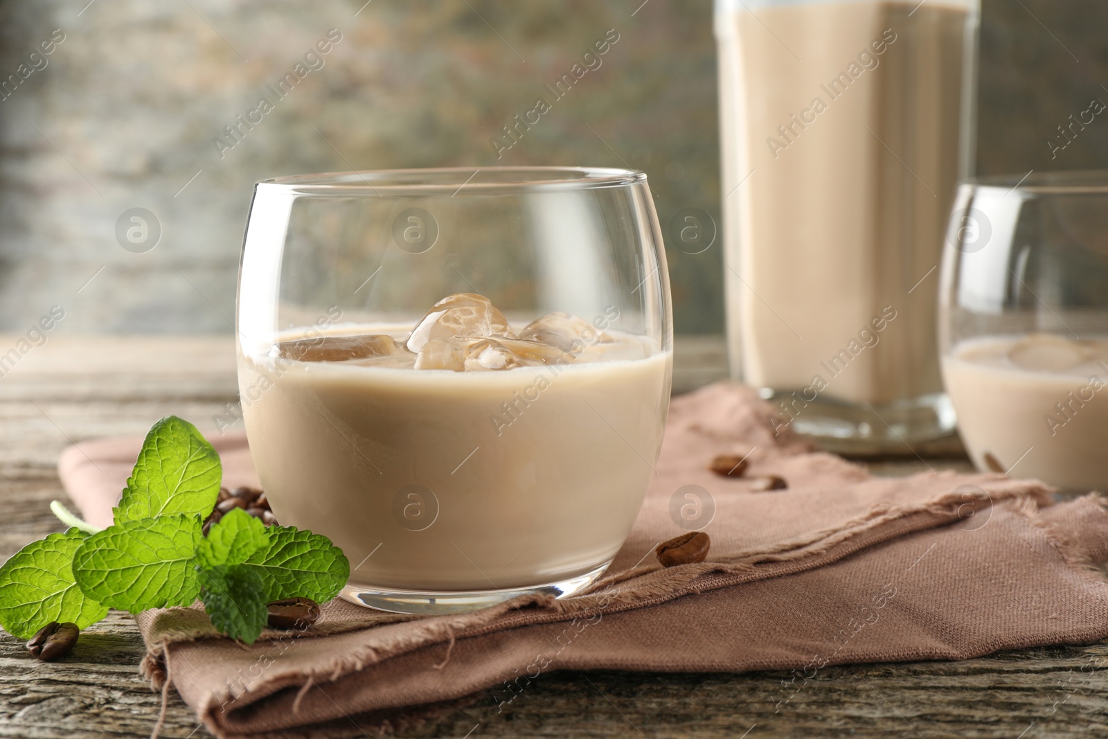 Photo of Coffee cream liqueur in glass, mint and beans on wooden table, closeup