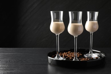 Photo of Coffee cream liqueur in glasses and beans on black wooden table, space for text