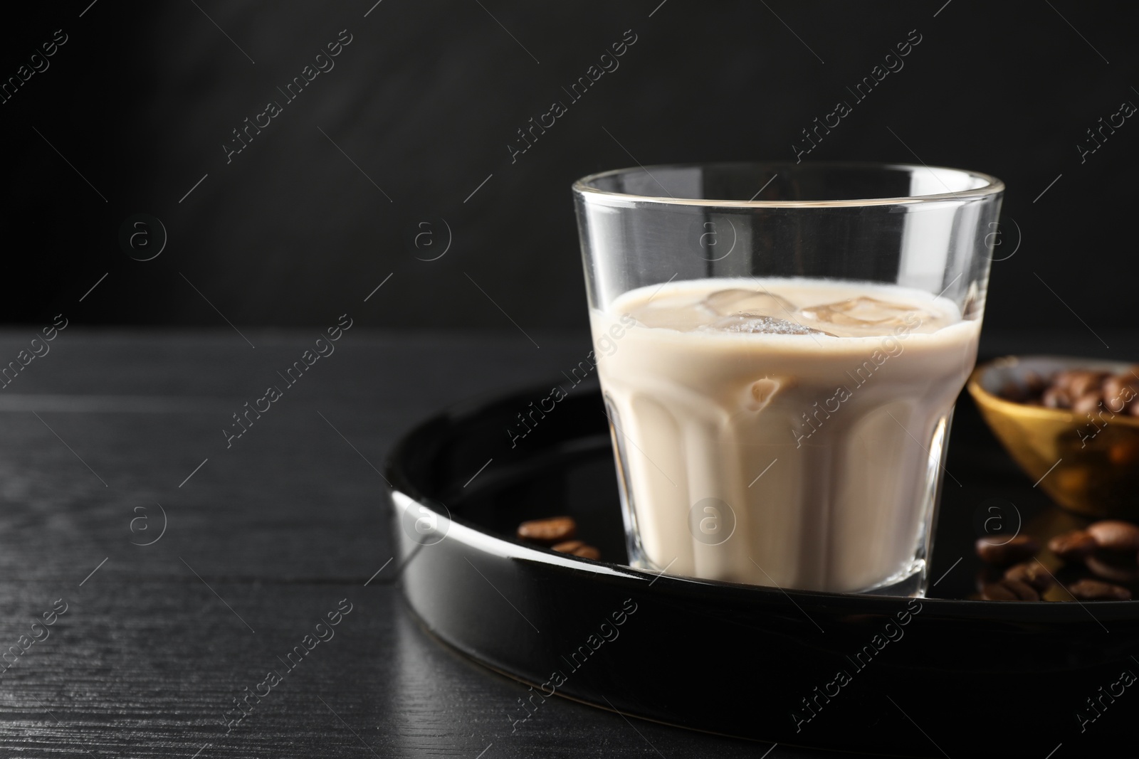 Photo of Coffee cream liqueur in glass and beans on black wooden table, space for text