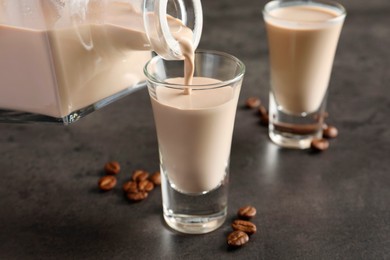 Photo of Pouring coffee cream liqueur into glass at grey table, closeup