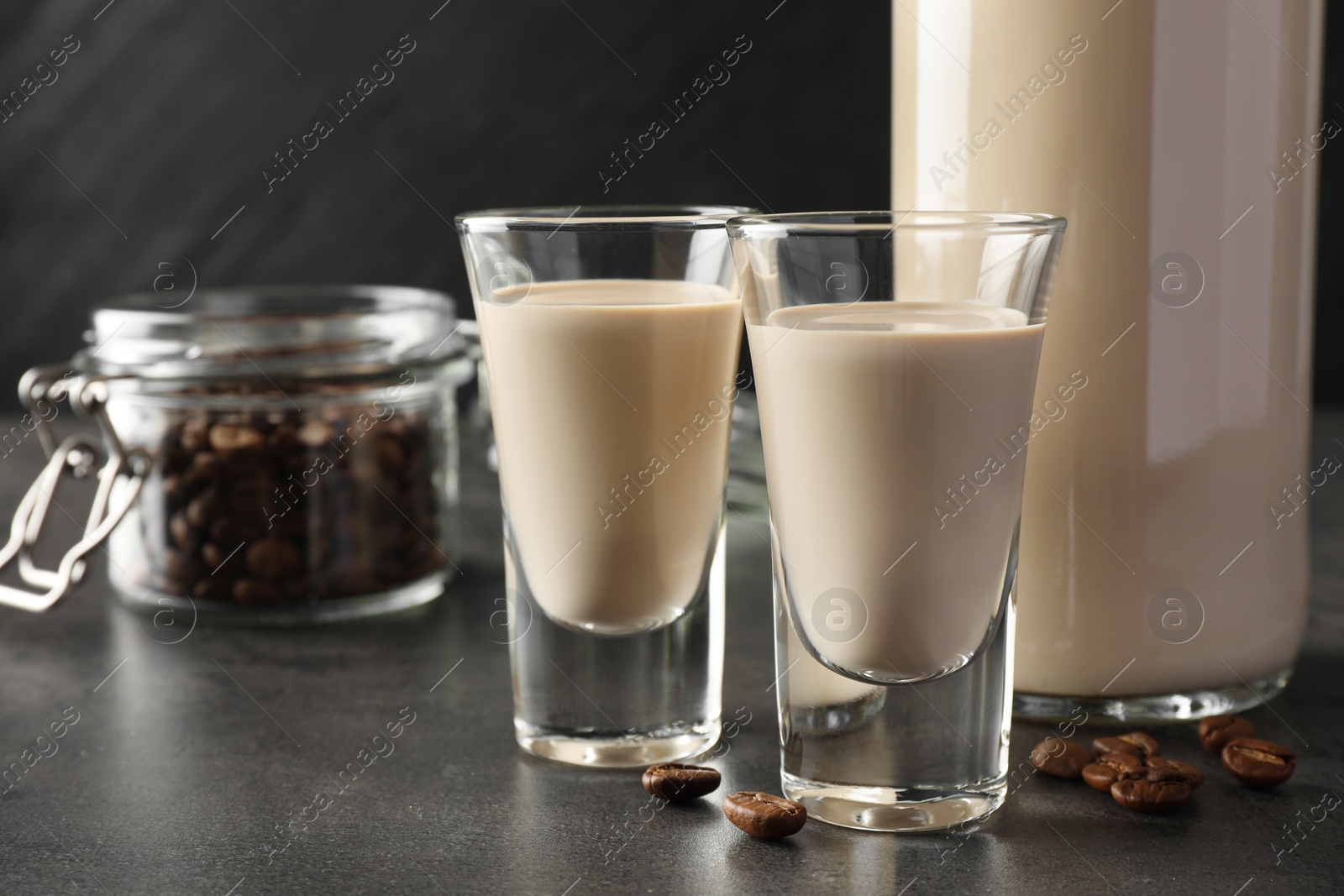 Photo of Coffee cream liqueur in glasses, bottle and beans on grey table, closeup