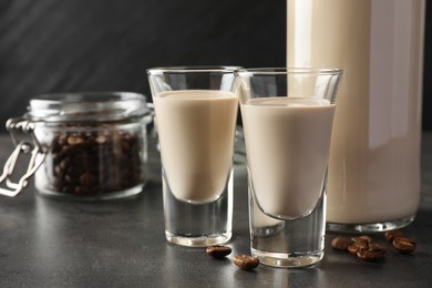 Photo of Coffee cream liqueur in glasses, bottle and beans on grey table, closeup