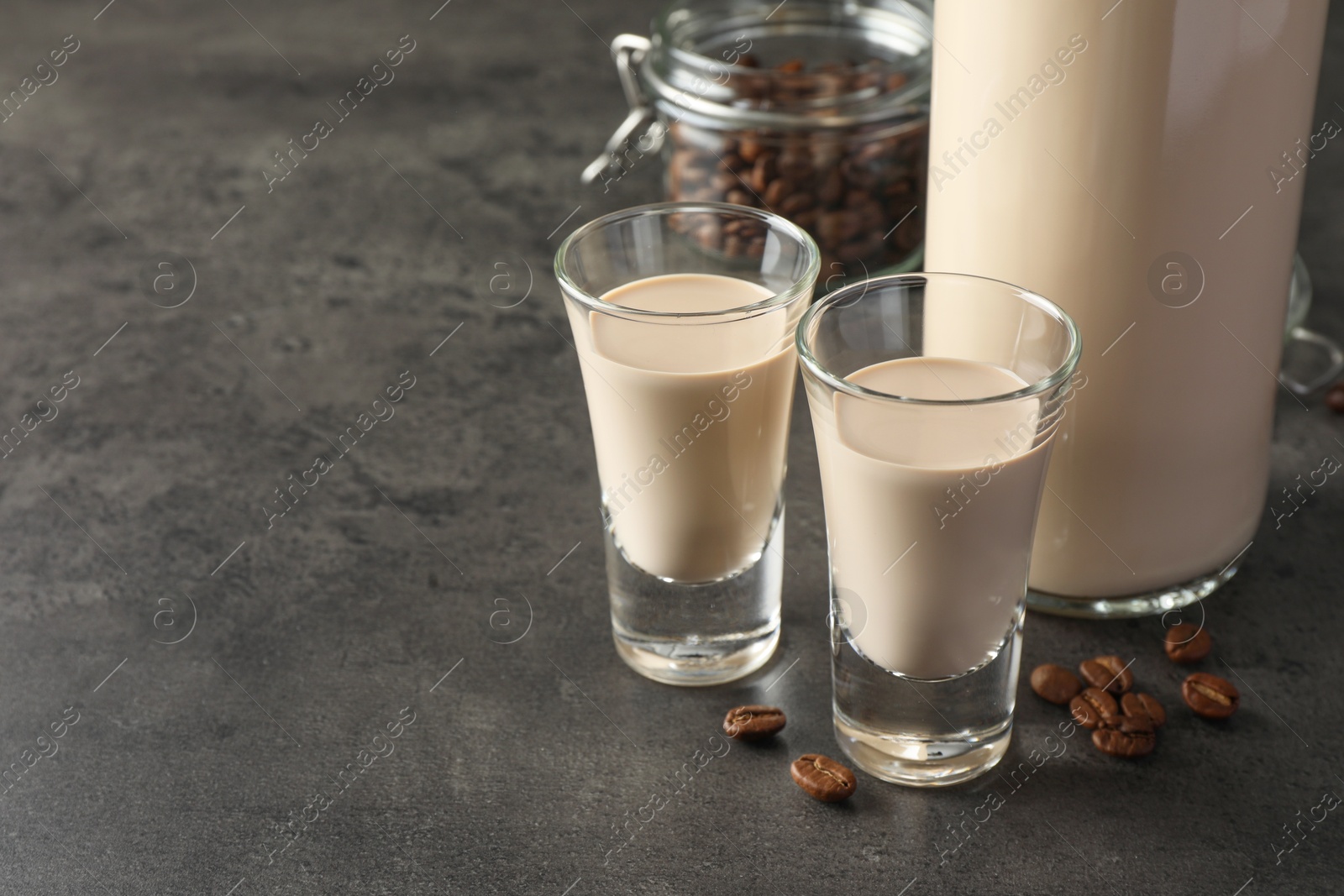 Photo of Coffee cream liqueur in glasses, bottle and beans on grey table, space for text