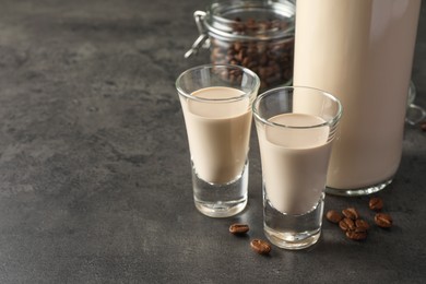 Coffee cream liqueur in glasses, bottle and beans on grey table, space for text