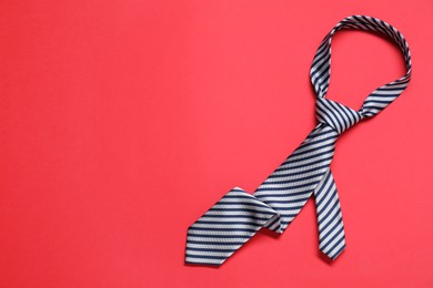 Photo of Striped necktie on red background, top view. Space for text