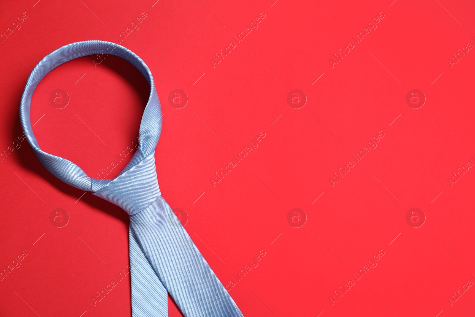 Photo of Light blue necktie on red background, top view. Space for text