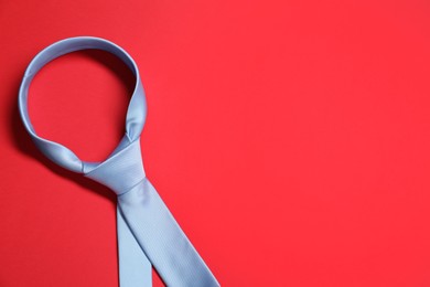 Photo of Light blue necktie on red background, top view. Space for text