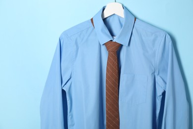 Photo of Hanger with shirt and brown necktie on light blue background