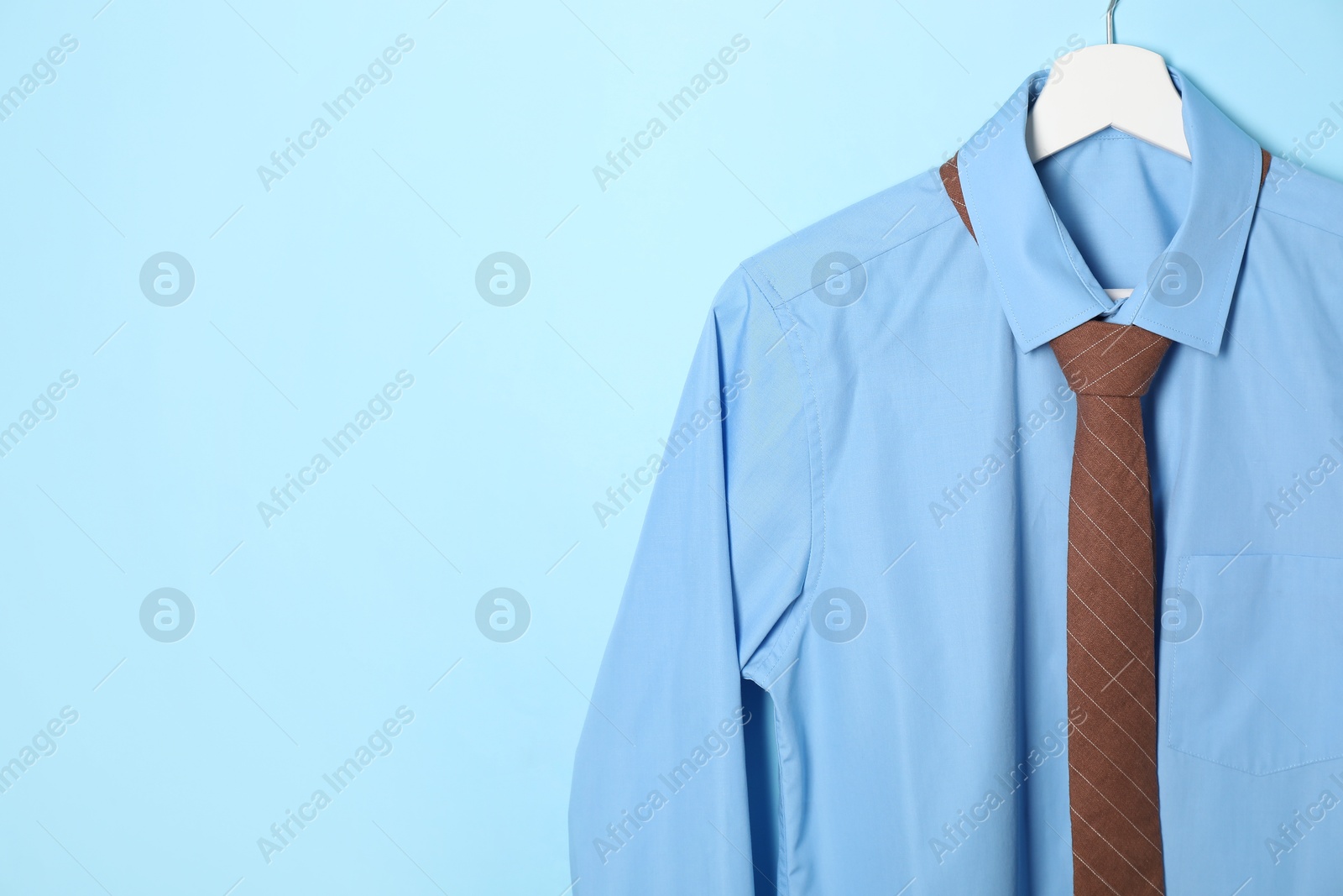 Photo of Hanger with shirt and brown necktie on light blue background. Space for text