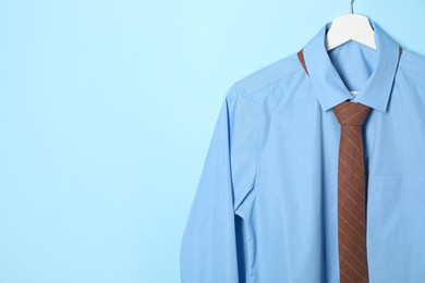 Photo of Hanger with shirt and brown necktie on light blue background. Space for text