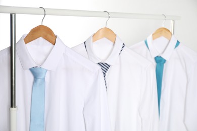 Hangers with white shirts and neckties on clothing rack against light background, closeup
