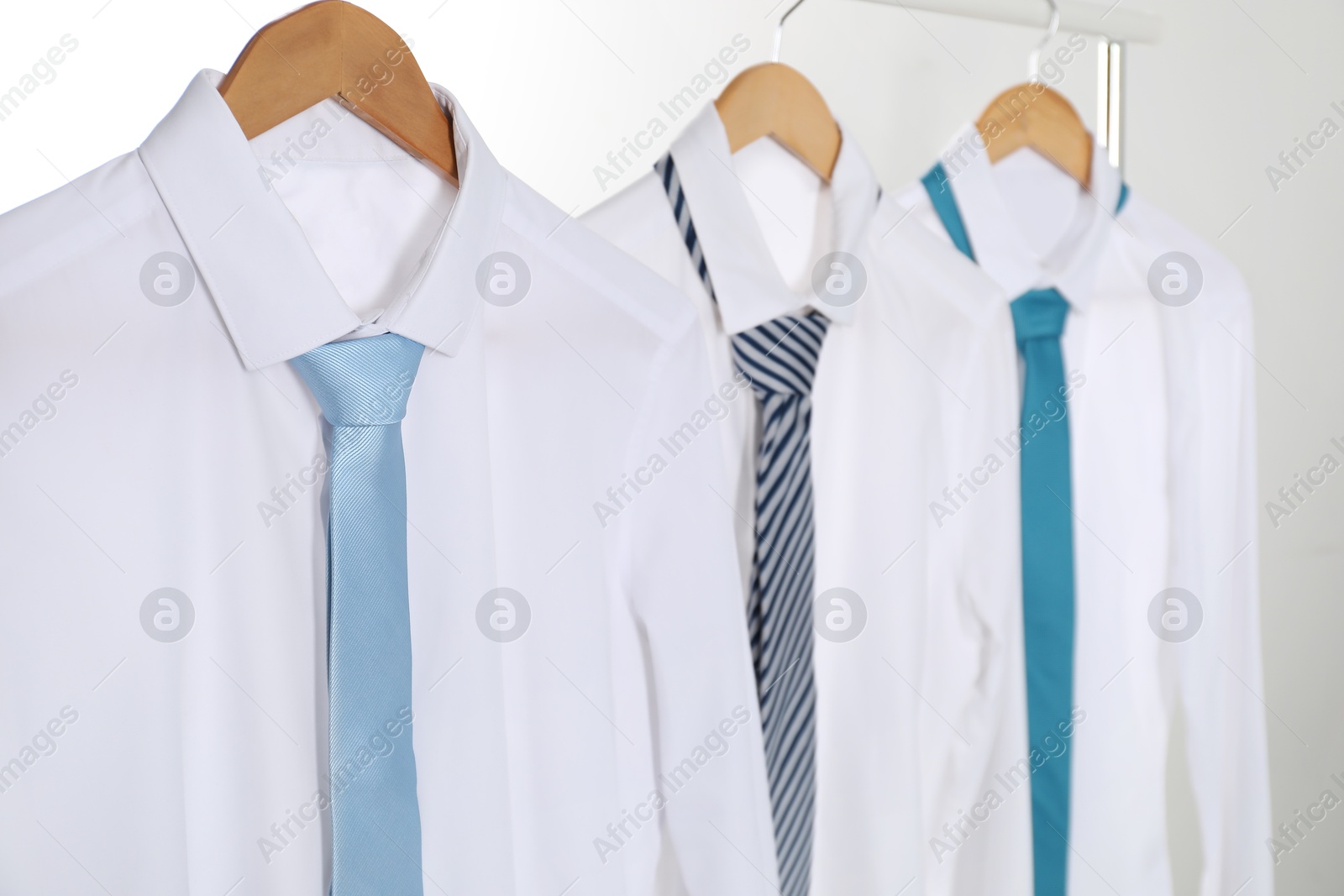 Photo of Hangers with white shirts and neckties on clothing rack against light background, closeup