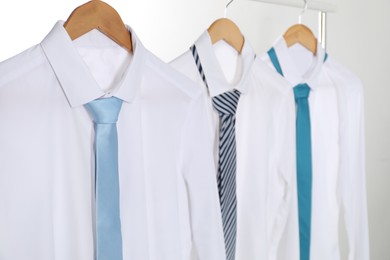 Photo of Hangers with white shirts and neckties on clothing rack against light background, closeup