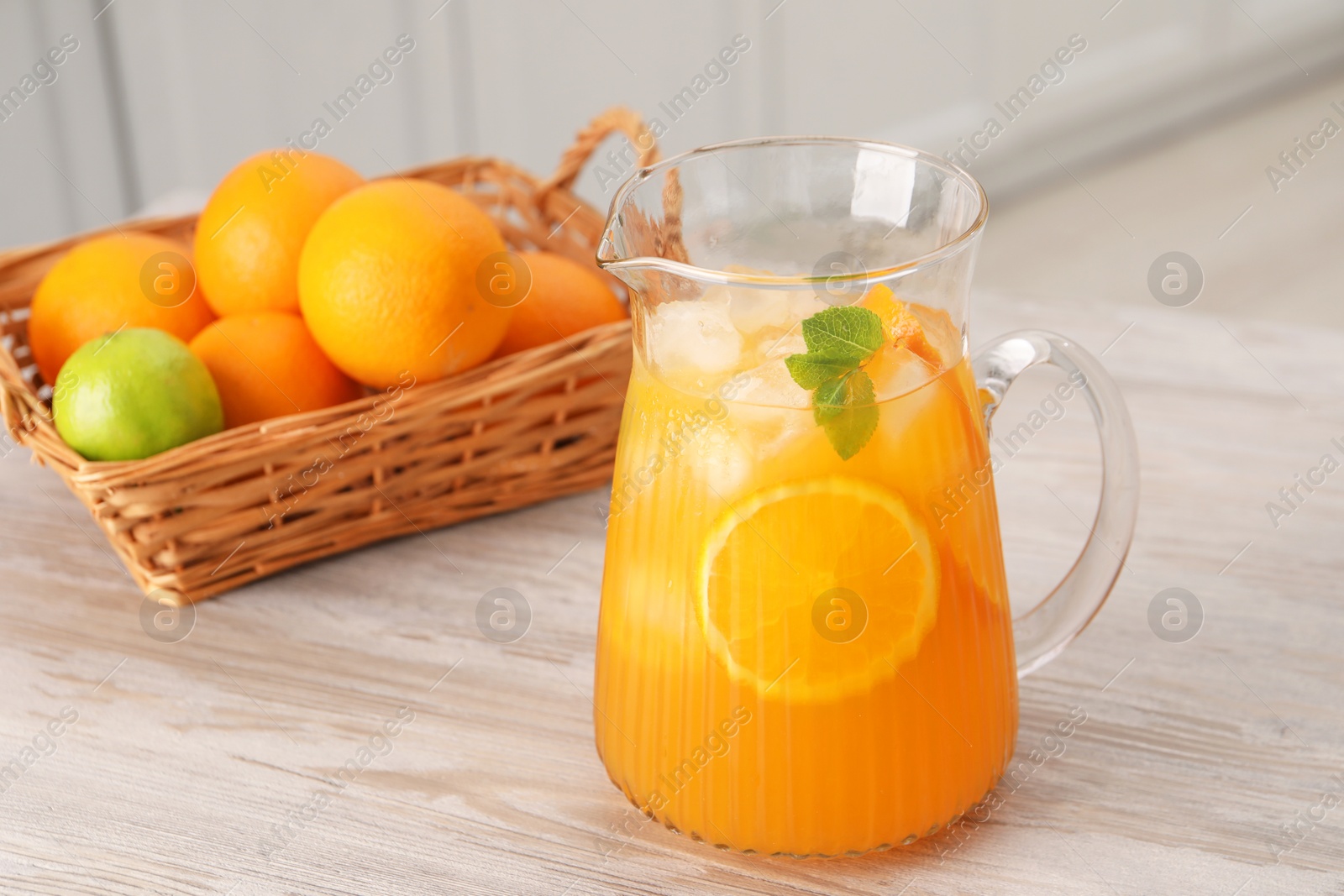 Photo of Freshly made lemonade in jug and citrus fruits on wooden table in kitchen