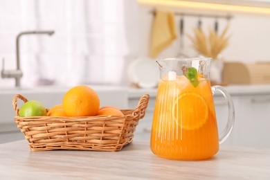 Photo of Freshly made lemonade in jug and citrus fruits on wooden table in kitchen