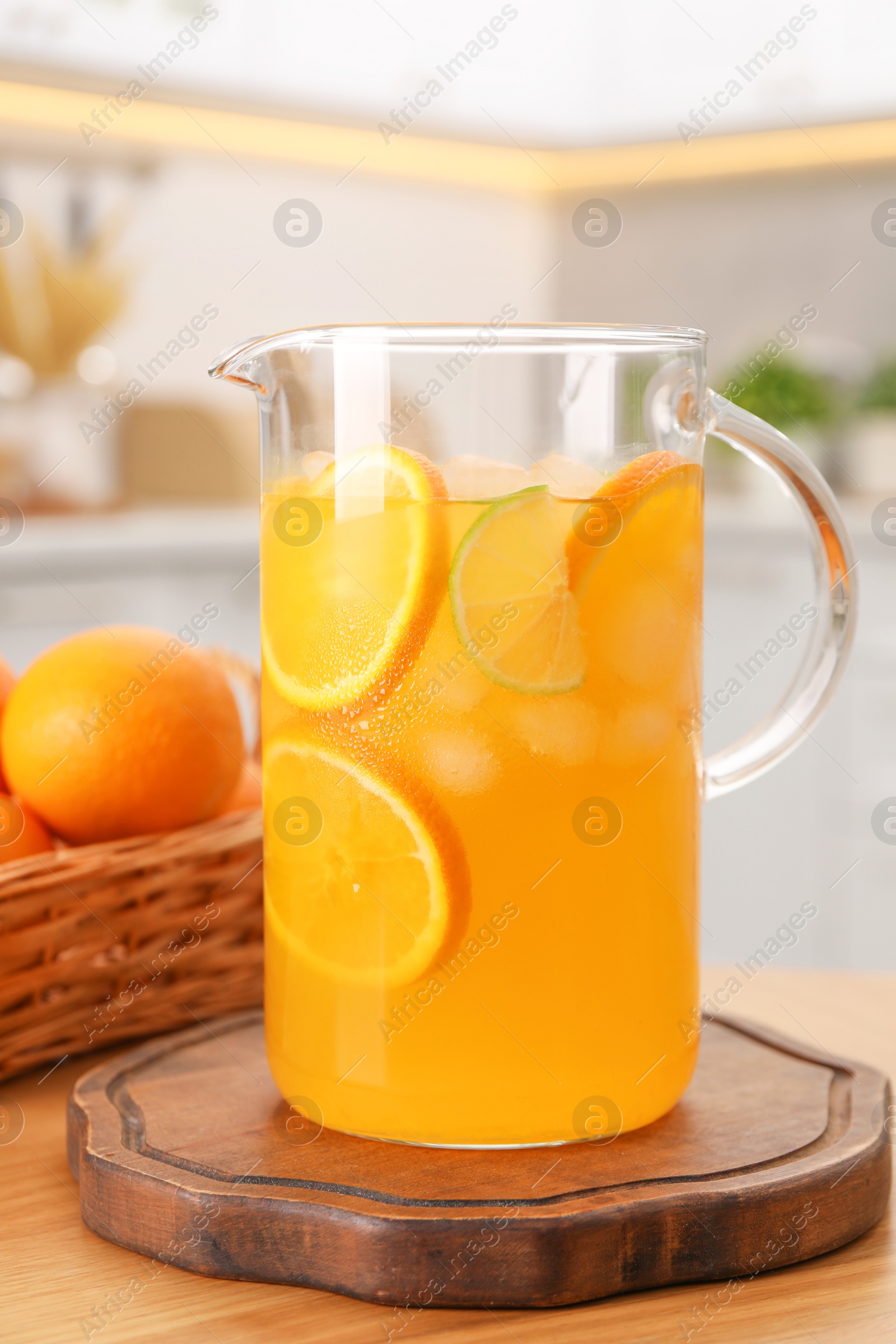 Photo of Freshly made lemonade in jug and citrus fruits on wooden table in kitchen