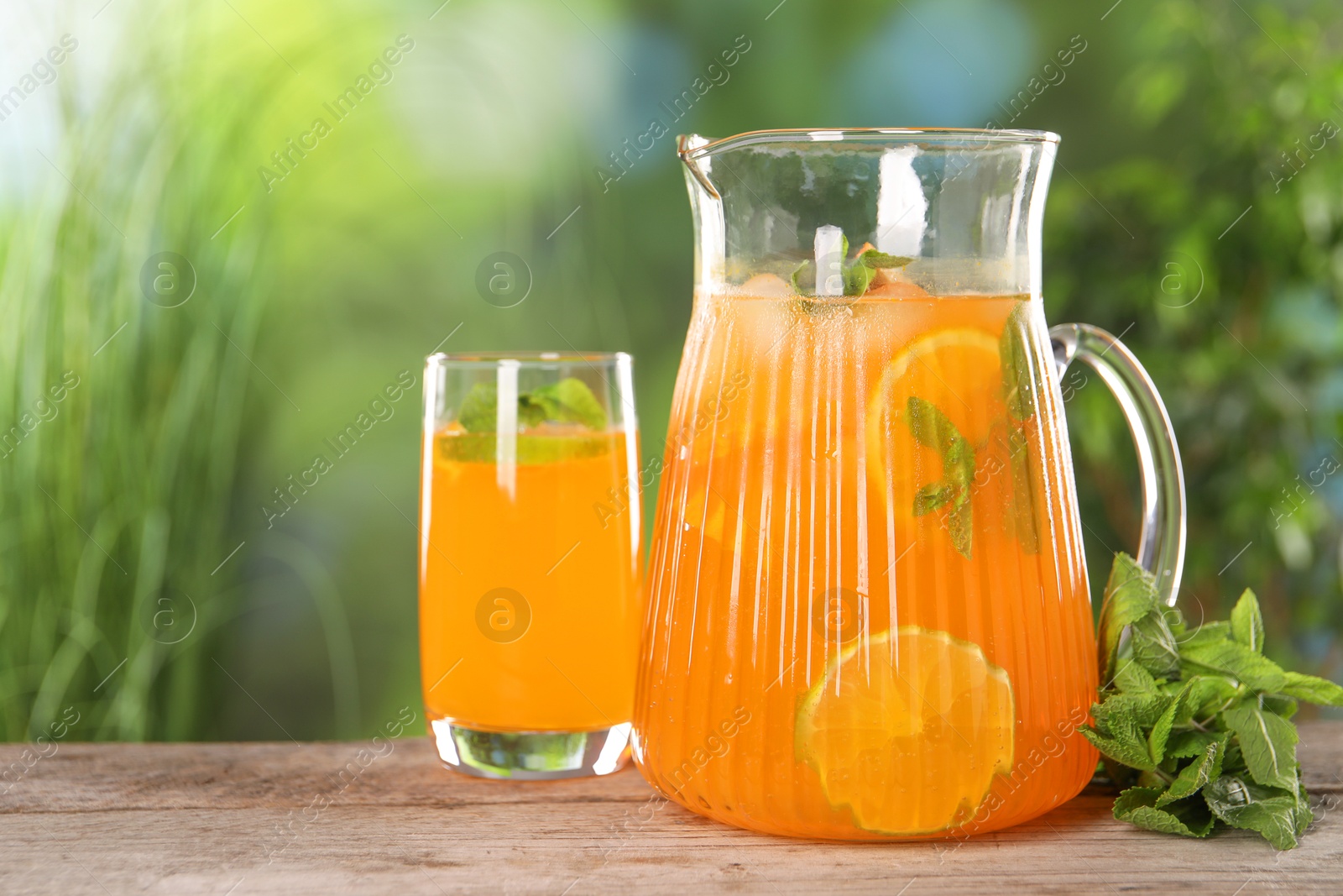 Photo of Freshly made lemonade in jug, glass and mint on wooden table outdoors, space for text