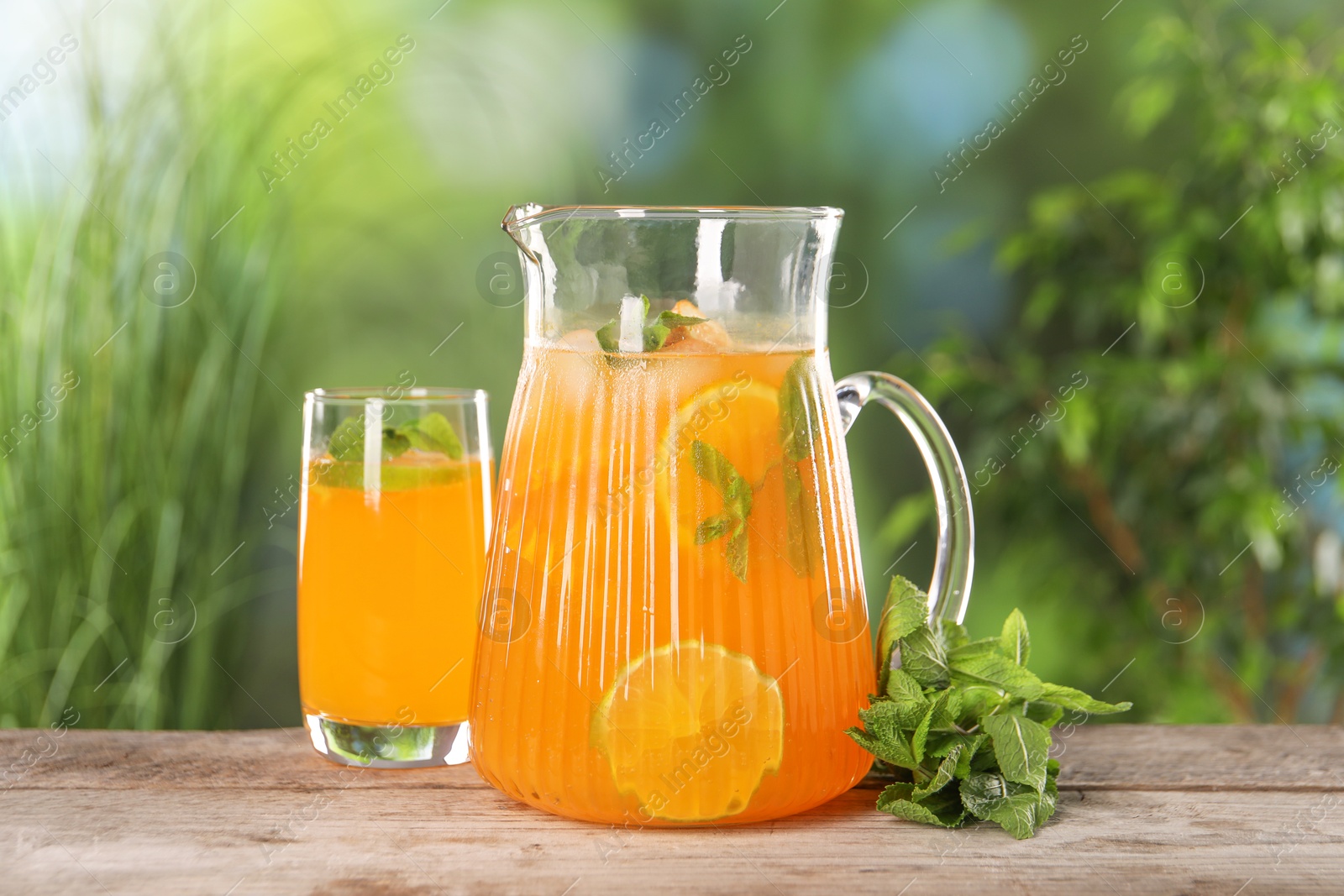 Photo of Freshly made lemonade in jug, glass and mint on wooden table outdoors