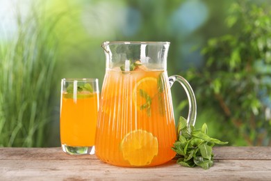 Freshly made lemonade in jug, glass and mint on wooden table outdoors