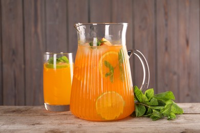 Photo of Freshly made lemonade in jug, glass and mint on wooden table