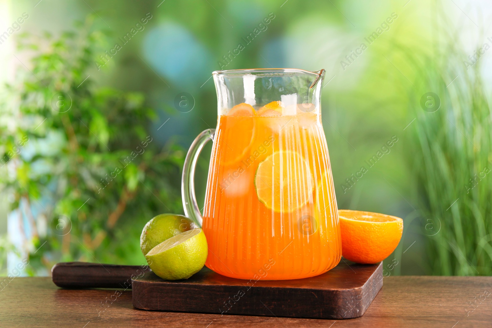 Photo of Freshly made lemonade in jug and citrus fruits on wooden table outdoors