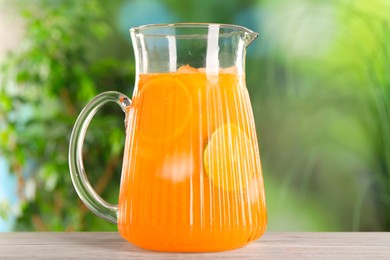 Photo of Freshly made lemonade in jug on wooden table outdoors