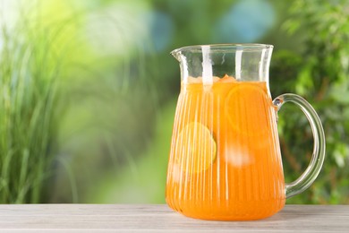 Freshly made lemonade in jug on wooden table outdoors, space for text