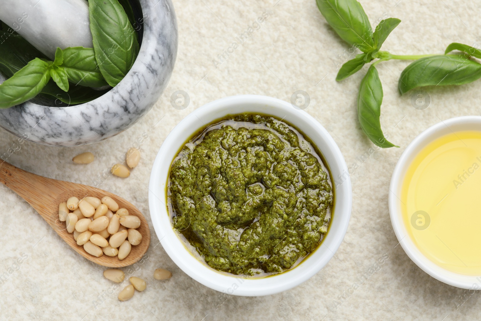 Photo of Tasty pesto sauce in bowl, basil, pine nuts and oil on light grey table, flat lay