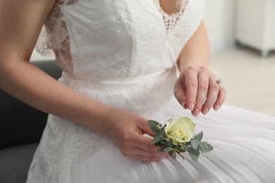 Bride holding boutonniere for her groom on blurred background, closeup