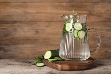 Photo of Refreshing cucumber water with rosemary in jug and vegetable on wooden table. Space for text