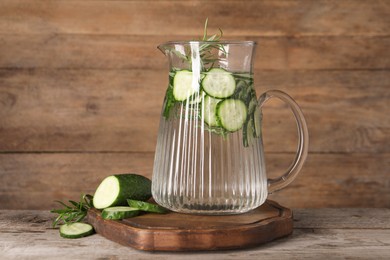 Photo of Refreshing cucumber water with rosemary in jug and vegetable on wooden table