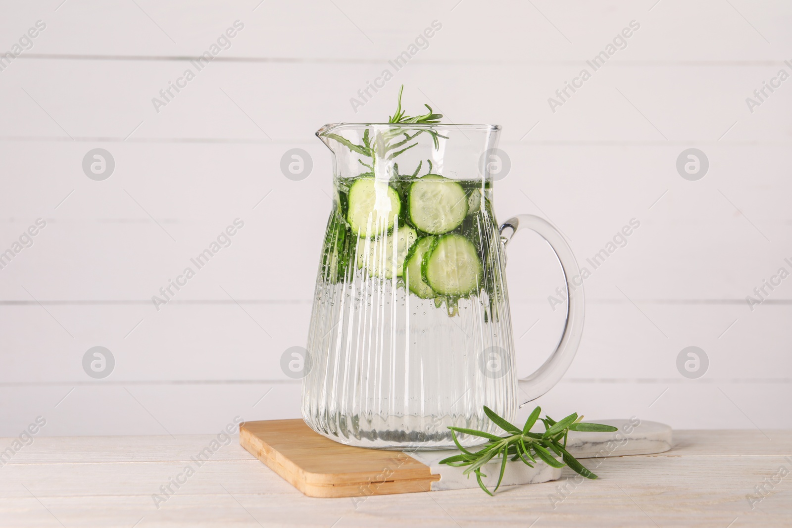 Photo of Refreshing cucumber water with rosemary in jug on light wooden table