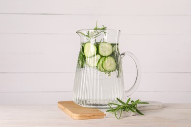 Refreshing cucumber water with rosemary in jug on light wooden table