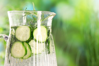 Photo of Refreshing cucumber water with rosemary in jug against blurred green background, closeup. Space for text