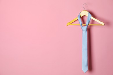 Hanger with light blue tie on pink background. Space for text