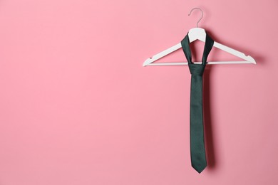 Photo of Hanger with black tie on pink background. Space for text