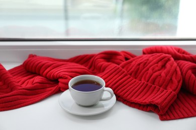 Photo of Red knitted scarf, hat, tea on windowsill